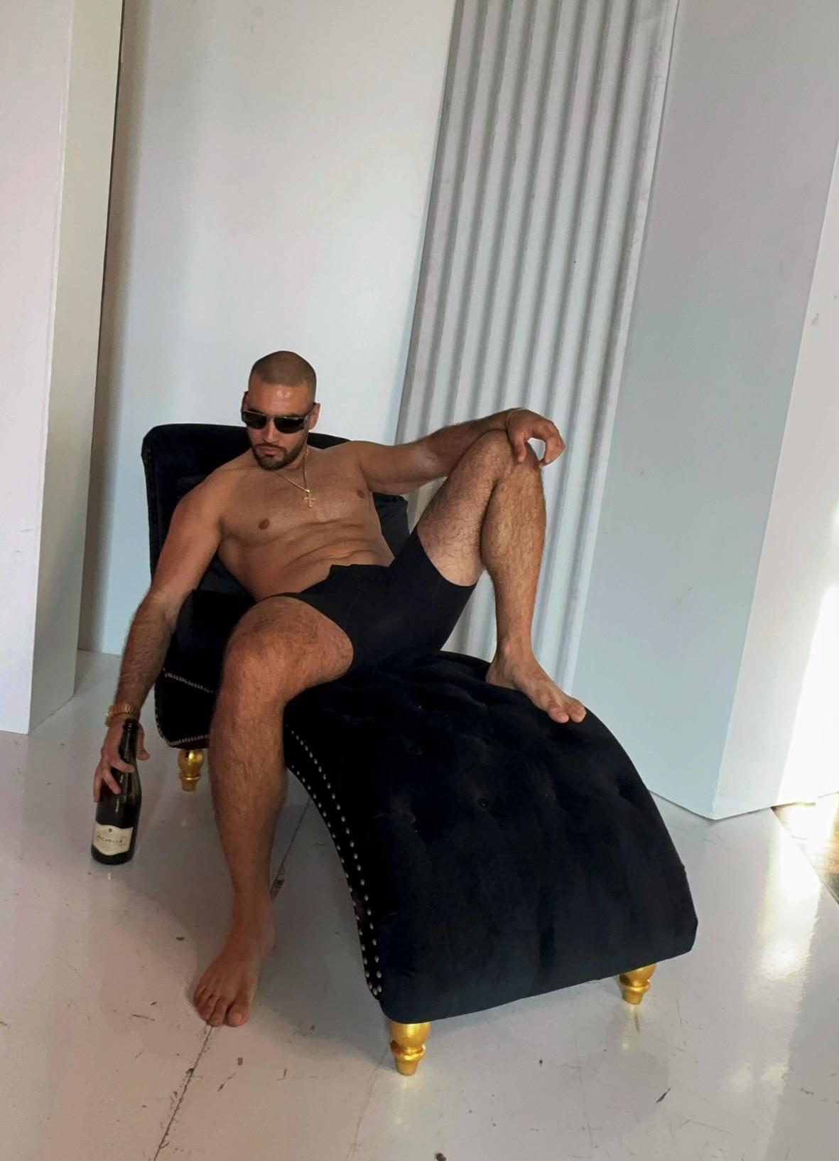 Dante reclining on a dark chaise with gold accents holding a bottle